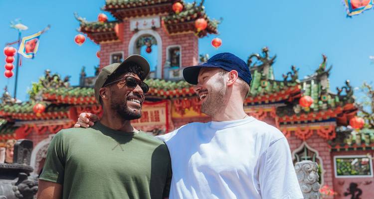 Twee vrienden lachen samen buiten een sierlijke tempel die versierd is met rode lantaarns.