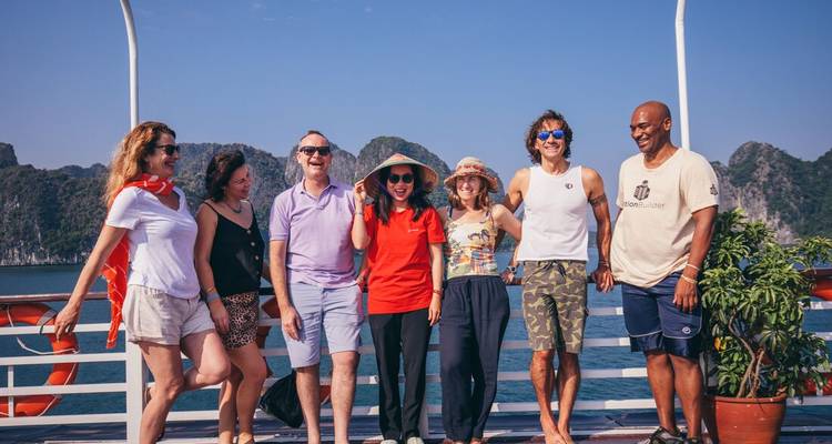 Reizigers poseren op het dek van een cruiseschip met de kalkstenen karsten van Halong Bay op de achtergrond.