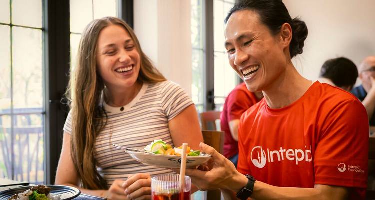 Twee reizigers lachen terwijl ze gerechten delen aan een restauranttafel.