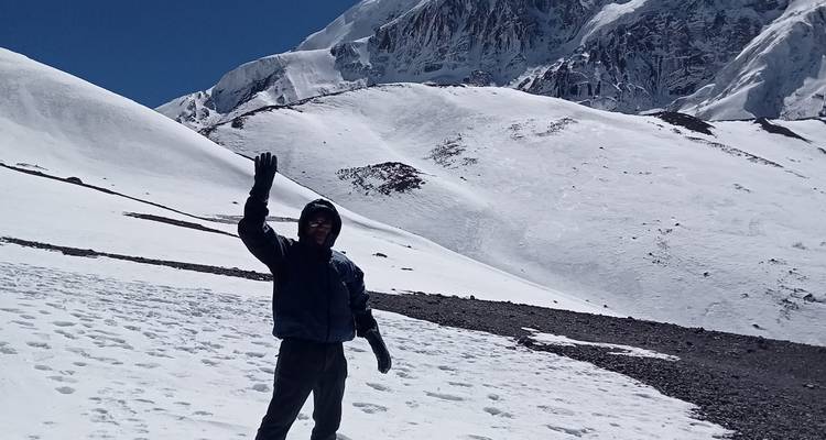 Randonneur agitant la main sur une crête himalayenne couverte de neige avec des pics imposants en arrière-plan.