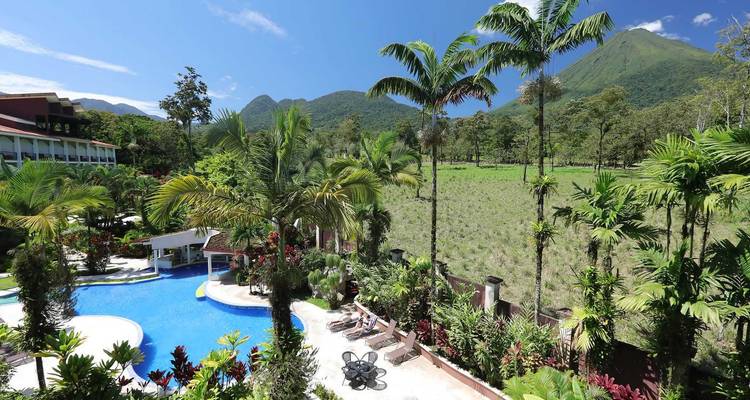 Complejo de piscinas del resort rodeado de jardines tropicales con el volcán Arenal elevándose en la distancia.