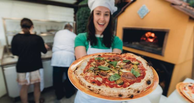 Chef joyeux en toque blanche présente une pizza fraîchement cuite garnie de basilic et de salami.