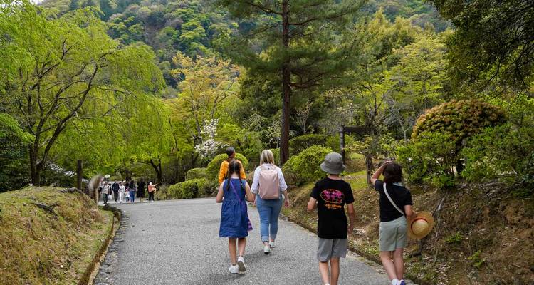 Un grupo familiar camina por un sendero boscoso rodeado del verdor fresco de la primavera en Arashiyama.