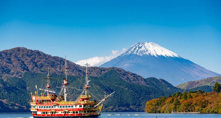 Un barco de avistamiento de estilo pirata rojo brillante navega por el Lago Ashi con el nevado Monte Fuji imponente de fondo.