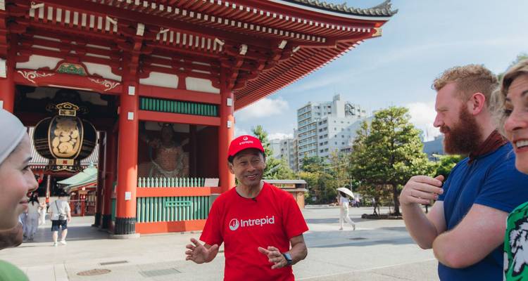 Un guía local con una camiseta roja de Intrepid explica la historia afuera del Templo Senso-ji mientras los viajeros escuchan.