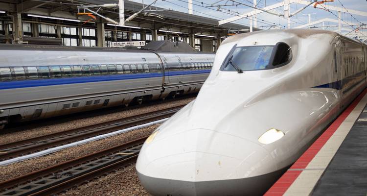 Un elegante tren bala shinkansen blanco espera en la plataforma junto a vagones plateados bajo los dosel de la estación.