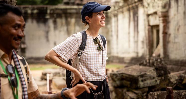 Un viajero sonriente que lleva una gorra escucha a un guía mientras explora las ruinas de un templo antiguo.