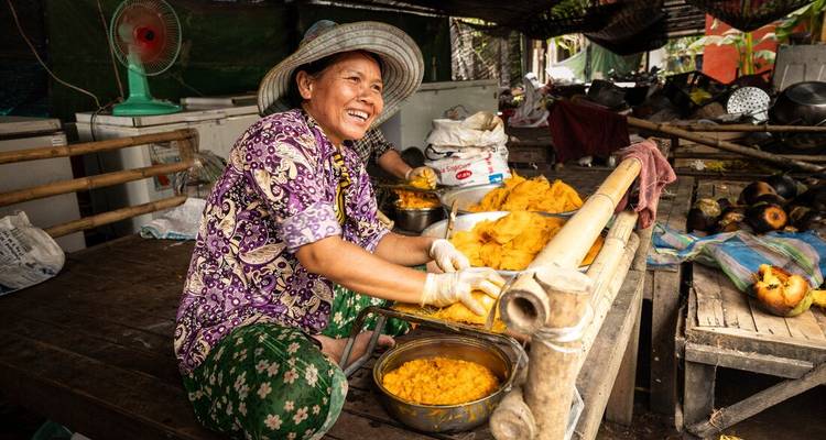 Un vendedor de mercado alegre con ropa estampada prepara pasta de curry naranja brillante en un puesto de madera rústica.