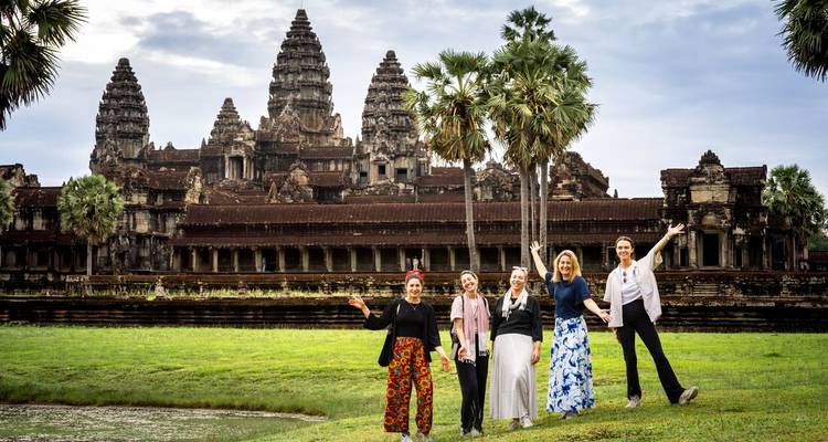 Cinco viajeros posan con entusiasmo frente a las icónicas torres de Angkor Wat en una mañana nublada.