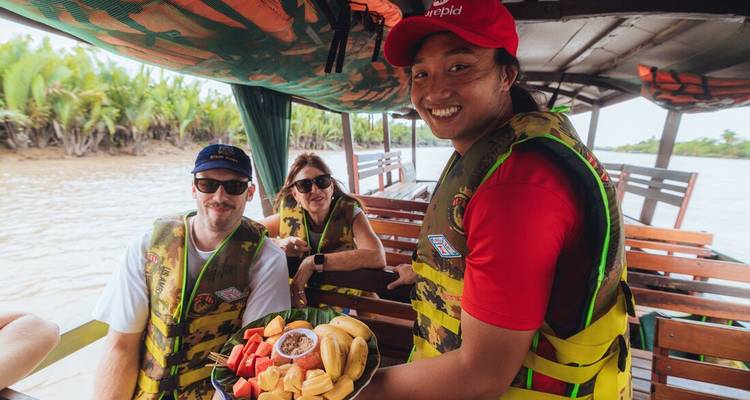 Un guide souriant offre un plateau de fruits tropicaux frais aux clients lors d'une excursion en bateau sur la rivière