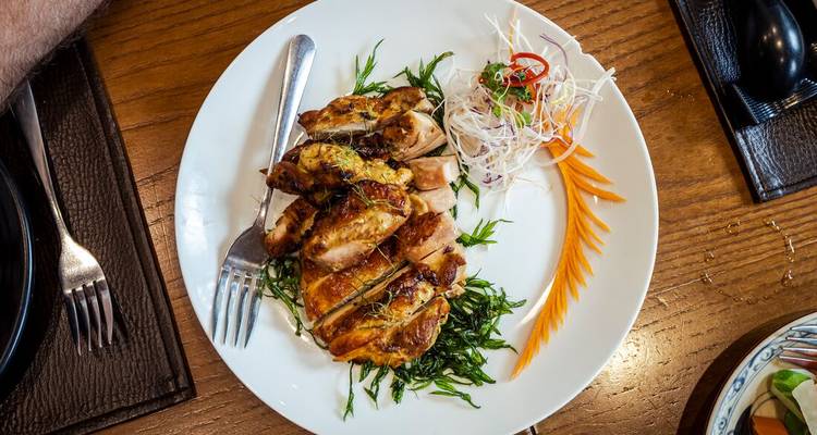 Poulet grillé en assiette garni d'herbes et de légumes en julienne sur une table en bois