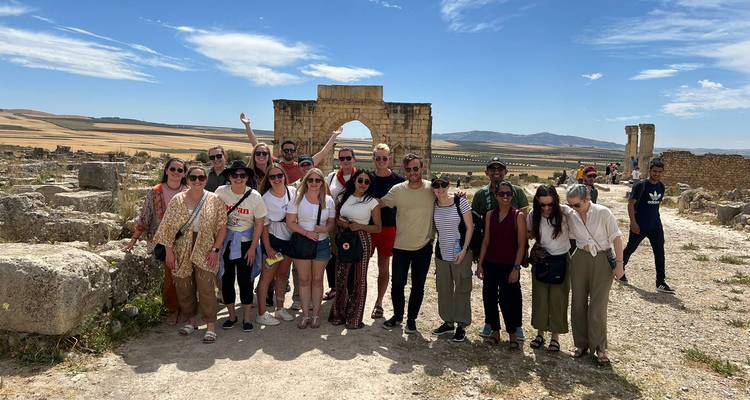 Groupe de personnes posant devant des ruines antiques sous un ciel bleu dégagé.