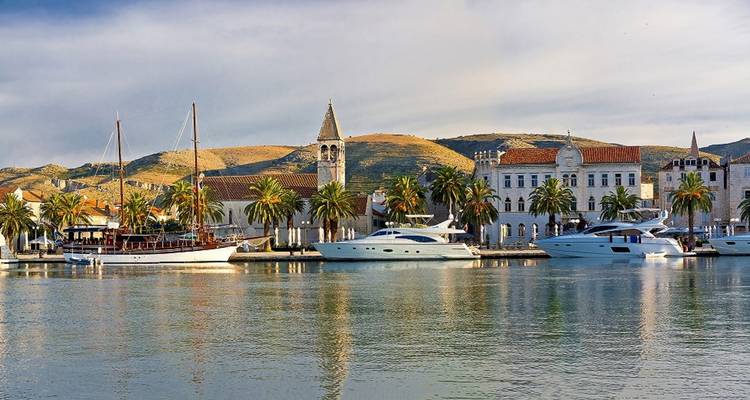 Vue côtière pittoresque d'une ville avec des yachts et des palmiers bordant la promenade.