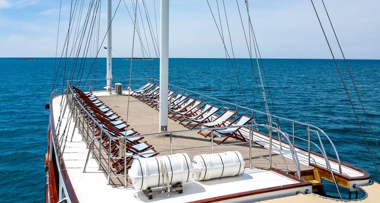 Deck area with sun loungers, surrounded by clear blue sea.