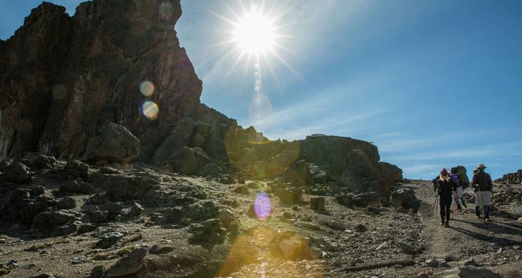 Les randonneurs traversent un sentier volcanique rocheux tandis que le soleil de midi crée de brillants halos lumineux.