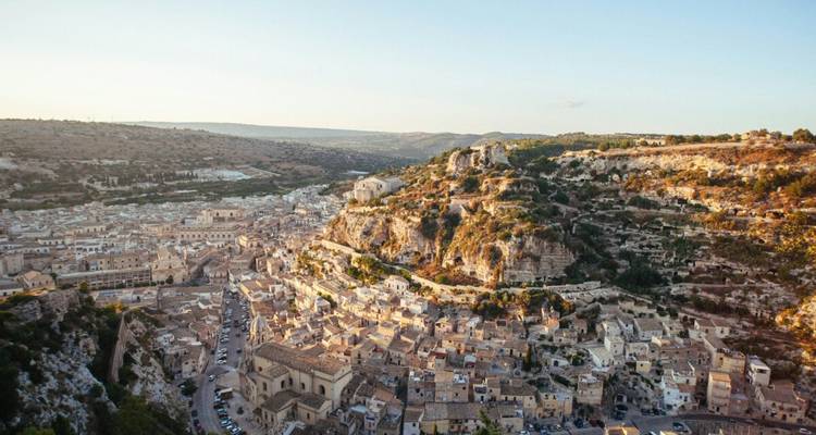 Vista aérea de la hora dorada de los tejados de terracota de Ragusa Ibla bajando en cascada por una colina hacia un valle profundo.