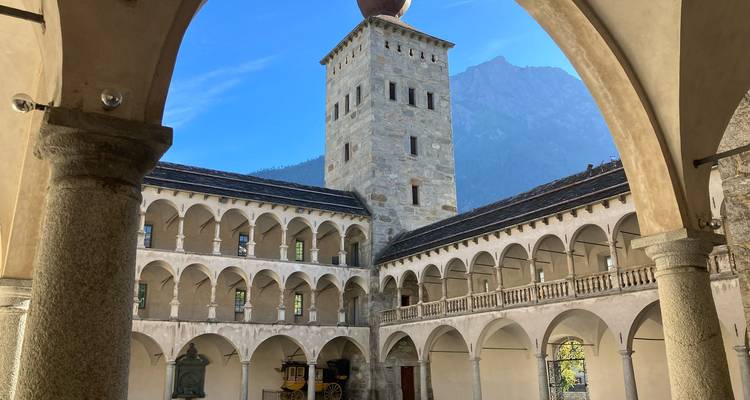 Historic arcaded courtyard of Stockalper Palace with mountain backdrop and clear blue sky.