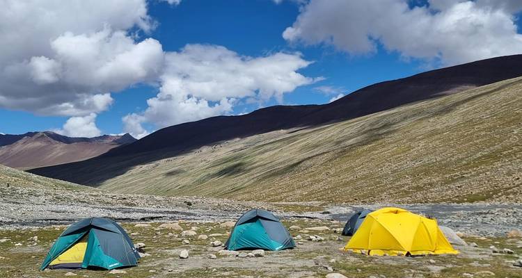 Tiendas de colores brillantes salpican un remoto valle alpino rodeado de laderas áridas y nubes dramáticas.