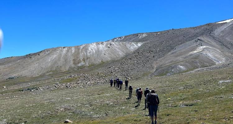 Los trekistas forman una línea a través de una cresta árida y alta hacia picos cubiertos de nieve.
