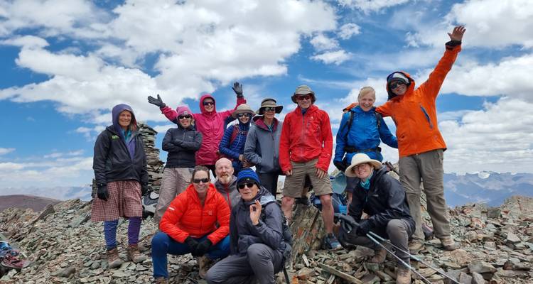 Grupo de alpinistas animándose en una cima rocosa bajo nubes dispersas y cordilleras escarpadas.
