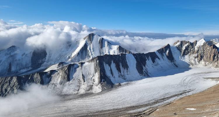 Los picos dentados cubiertos de nieve se elevan sobre nubes arremolinadas y una vasta cuenca glaciar.