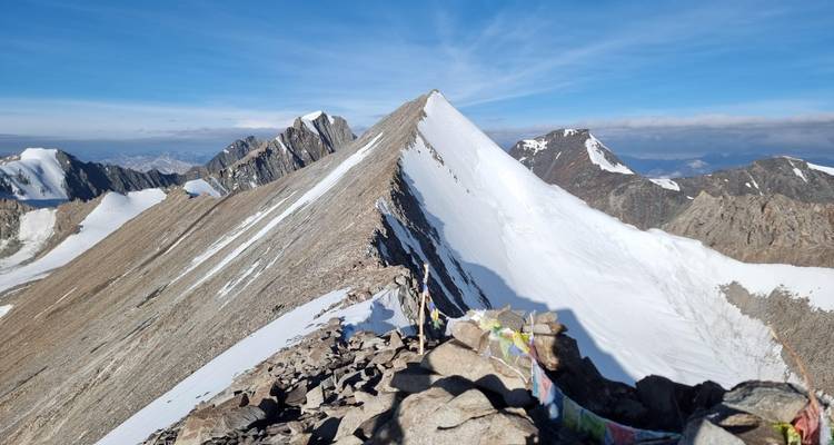 Una cresta afilada cubierta de nieve te lleva a una cumbre puntiaguda rodeada de cadenas montañosas escarpadas en un día despejado.