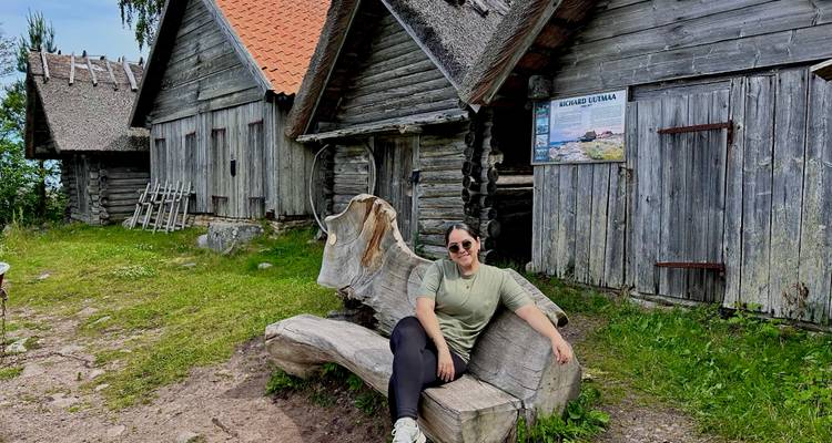 Une femme se détend sur un banc en forme de tronc d'arbre sculpté à côté de cabanes côtières rustiques.