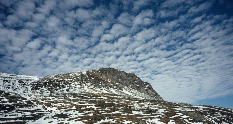 Cresta nevada bajo un cielo dramático lleno de nubes altocúmulos con patrones.