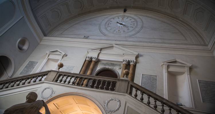 Un élégant escalier en marbre avec des colonnes classiques et un plafond en rose des vents orne un intérieur historique.