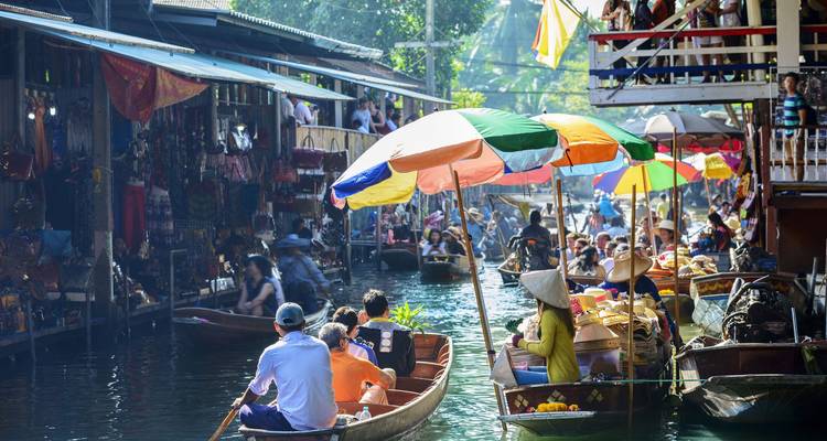 Mercado flotante bullicioso con muchos botes de madera que llevan sombrillas coloridas, productos frescos y vendedores remando por un canal estrecho.