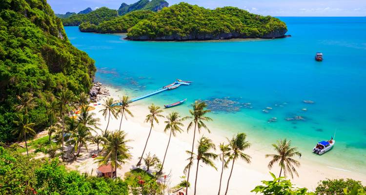 Bahía turquesa con playa de arena blanca bordeada de palmeras y botes de cola larga en el Parque Marino Mu Koh Angthong.