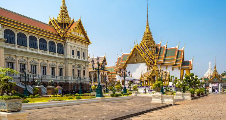 Complejo del Gran Palacio en Bangkok con tejados dorados ornamentados, agujas y patios cuidadosamente mantenidos bajo cielos azules despejados.