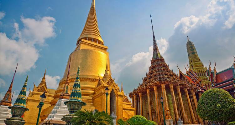 Imponentes stupas doradas y templos ornamentados de Wat Phra Kaew brillando contra un cielo parcialmente nublado.