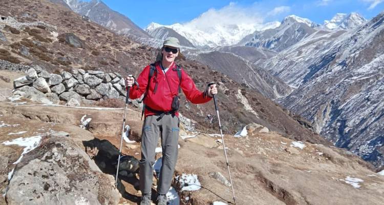 Wandelaar met trekkingstokken staat op een robuust pad met sneeuwbedekte Himalaya-toppen op de achtergrond.