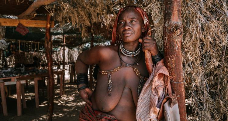 Portret van een persoon die traditionele kleding draagt en onder een baldakijn staat.