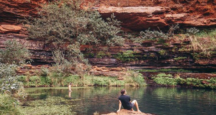 Los visitantes se refrescan en una poza esmeralda apartada bajo imponentes acantilados rojos.