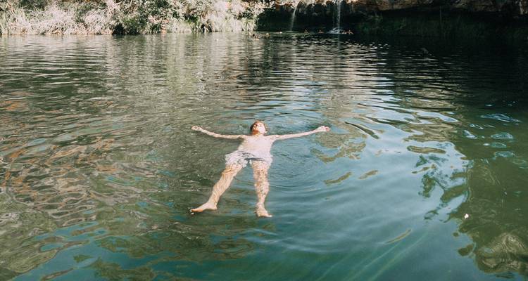 Un viajero flota tranquilamente boca arriba en una piscina natural calmada rodeada de vegetación.