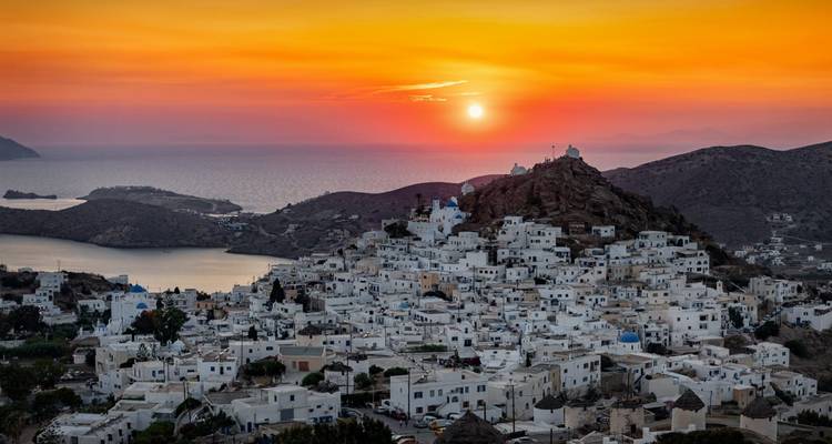 Una vista impresionante del atardecer sobre un pueblo montañoso con edificios blancos, posiblemente en Grecia.