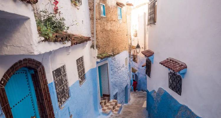 Narrow blue-and-white alley with stairs and colorful doors in Chefchaouen's medina.