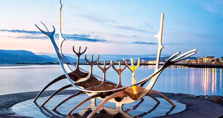 Artistic Sun Voyager sculpture beside calm waters with pastel evening sky and distant lights of Reykjavik.