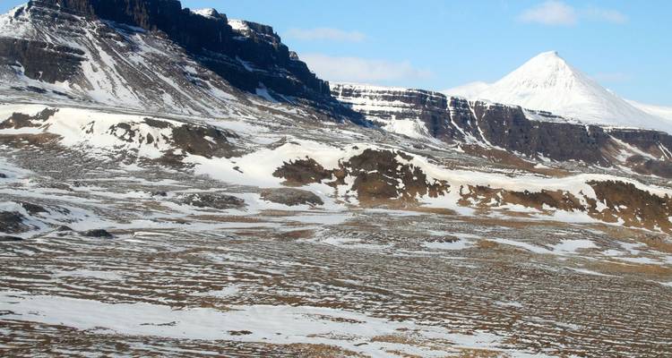 Snow-covered volcanic ridges contrasting with brown tundra plains under bright winter light.