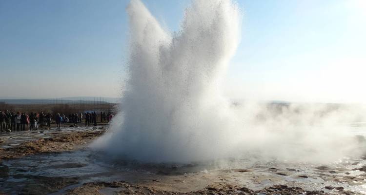 Un geyser en éruption avec une foule qui l'observe à distance.