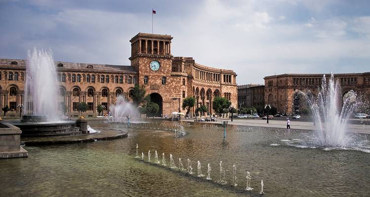 Grand central square with dancing fountains in front of ornate pink-stone government buildings.