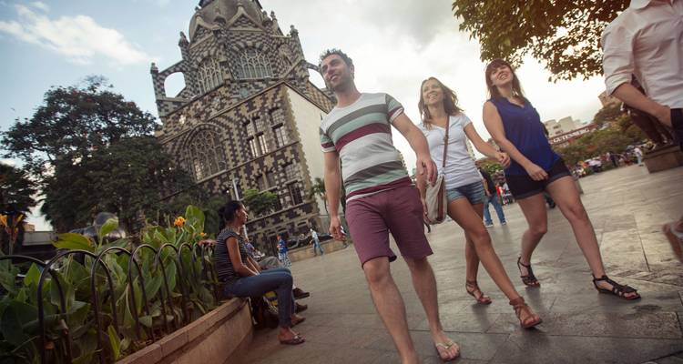Travelers walking through a lively city square beside an ornate stone building with unique patterned facade.