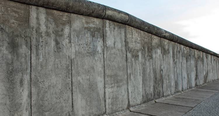 Perspectiva de primer plano de una sección de hormigón desnudo del Muro de Berlín contra un cielo pálido.