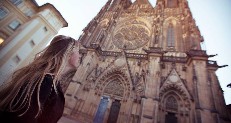 Mujer joven mirando hacia arriba la fachada ornamentada de la Catedral de San Vito de Praga desde muy cerca.