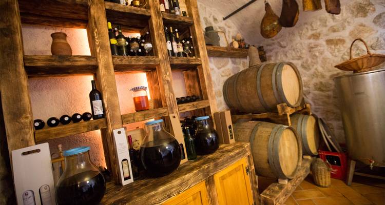 Rustic stone wine cellar with wooden shelves of bottles and large aging barrels.
