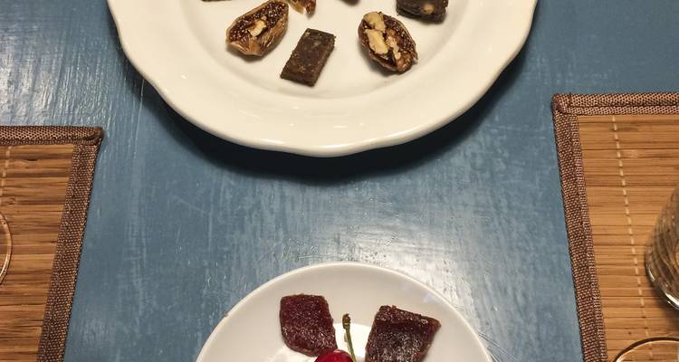 Small dessert portions and a cherry presented on white plates atop a blue table.