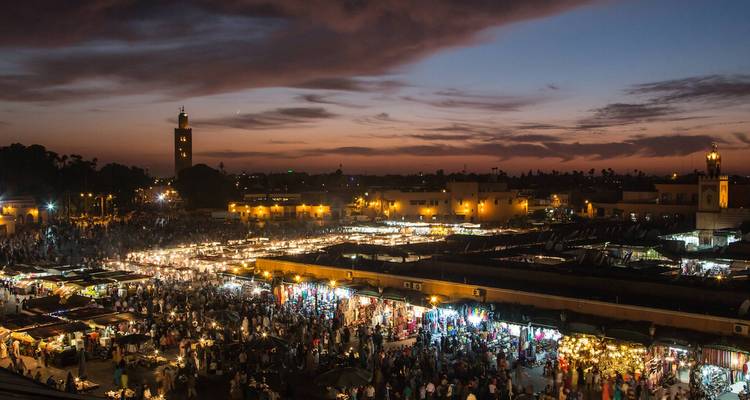 Sweeping twilight view over Marrakesh’s buzzing Jemaa el-Fnaa square packed with illuminated stalls and crowds.