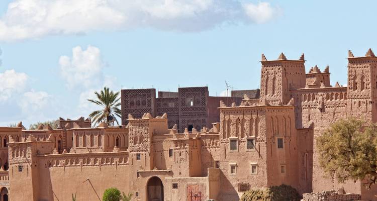 Earthen ramparts and towers of the famous kasbah of Aït Benhaddou under a bright morning sky.